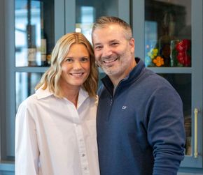Woman and man smiling, standing close together in front of a blue cabinet.