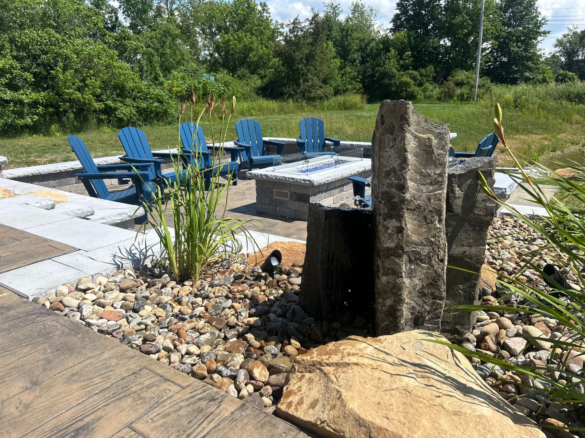 Outdoor seating area with blue chairs, fire pit, and a water feature.