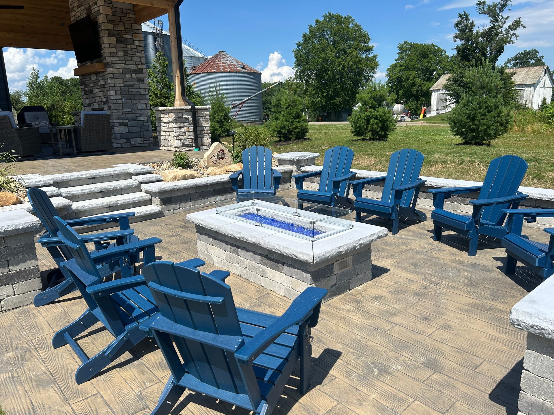 Outdoor seating area with blue chairs around a fire pit on a patio.
