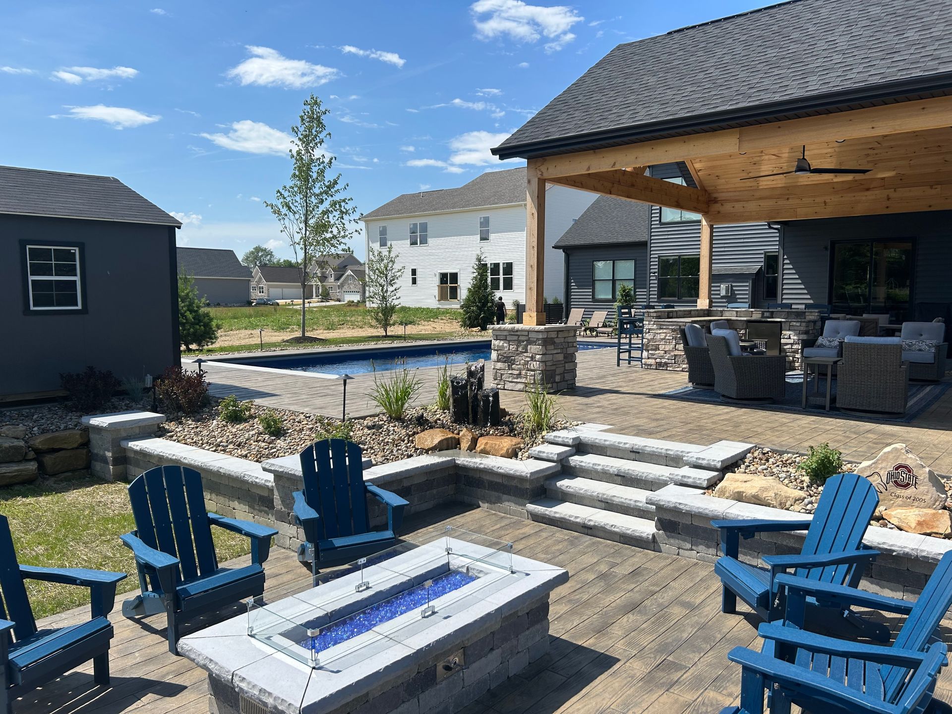 Outdoor patio with blue chairs, fire pit, swimming pool, and covered seating area.