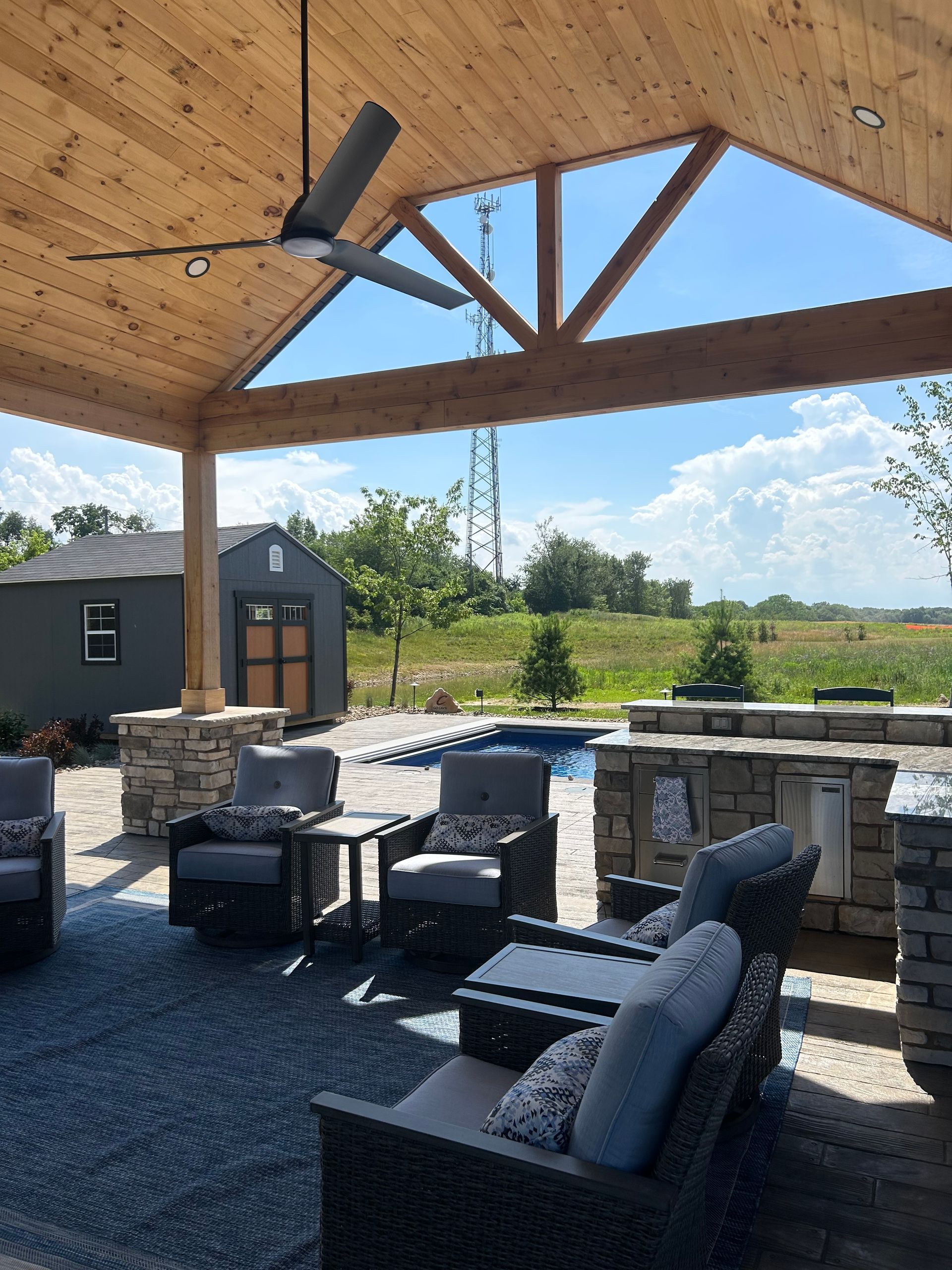 Patio with wood ceiling, seating, and outdoor kitchen overlooking a pool and landscape.