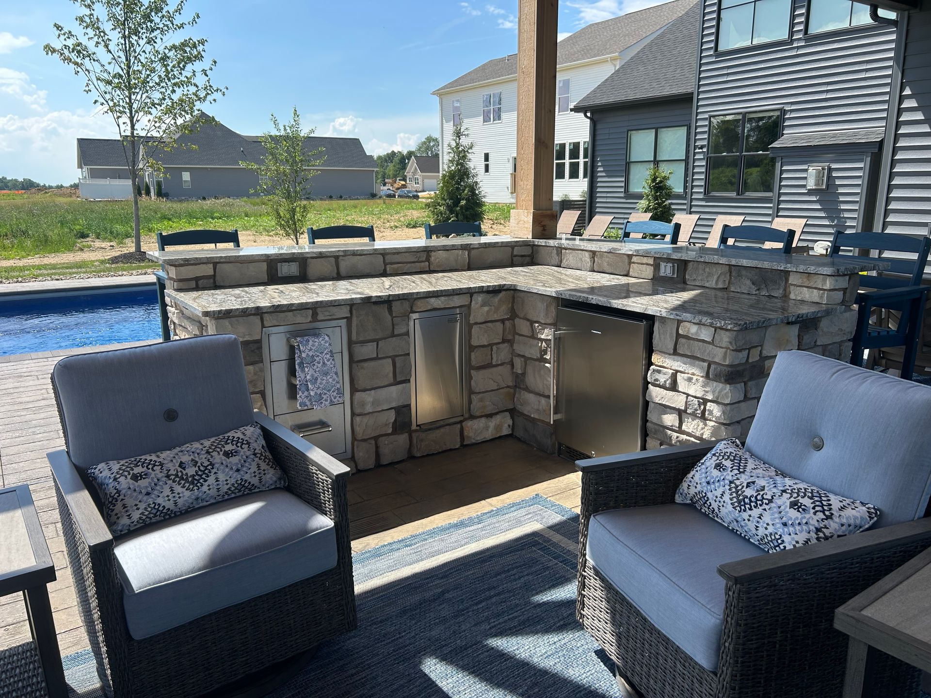 Outdoor kitchen with stone, stainless steel appliances, and seating on a patio.