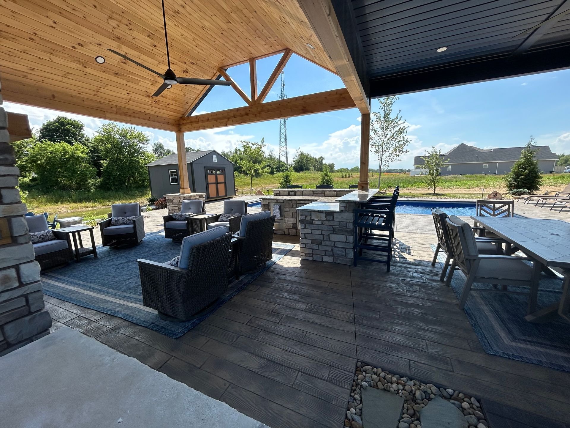 Covered patio with seating areas, bar, and dining, with a pool and fields in the distance.