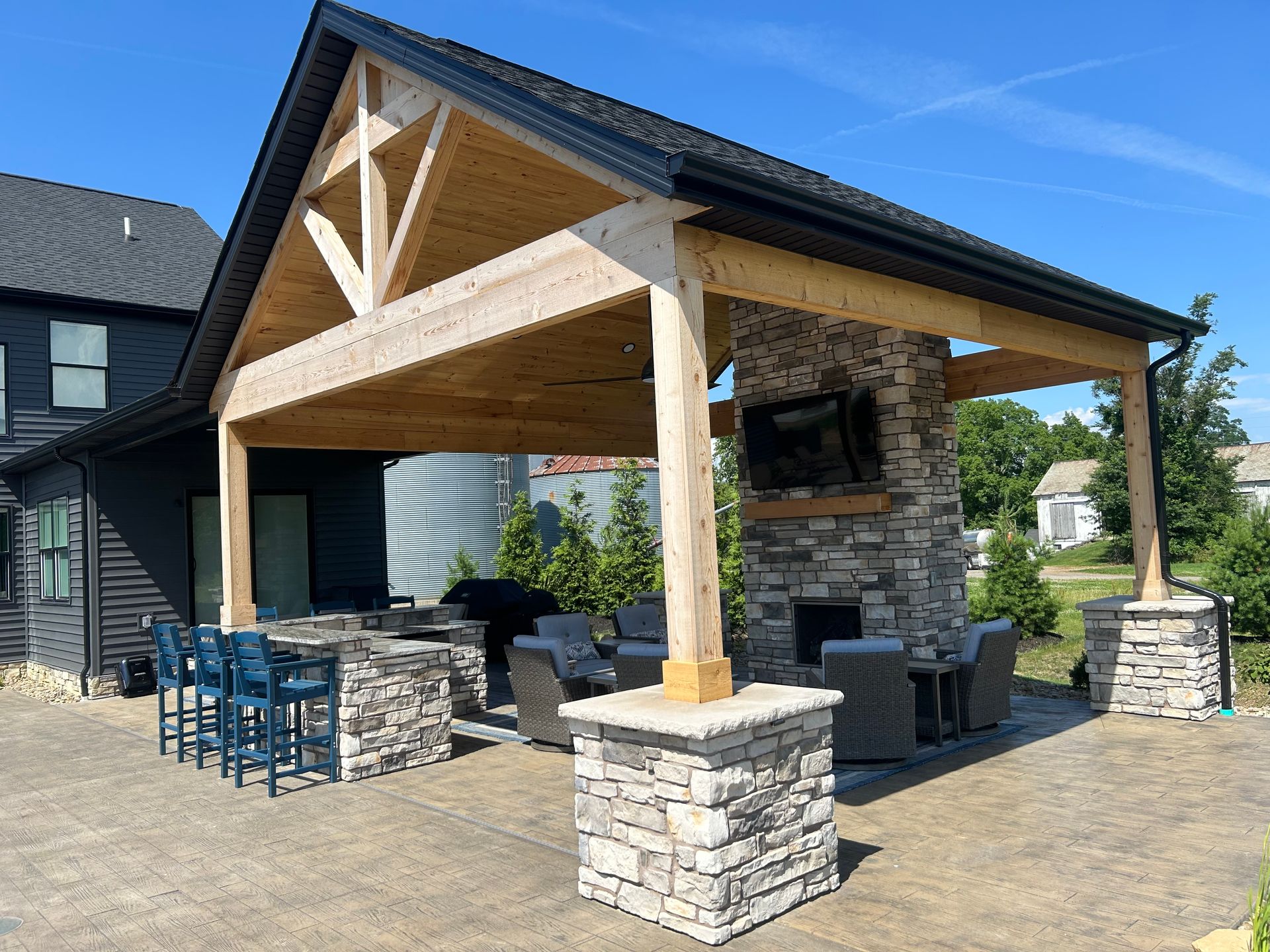Outdoor covered patio with stone fireplace, bar, seating, and a mounted TV.