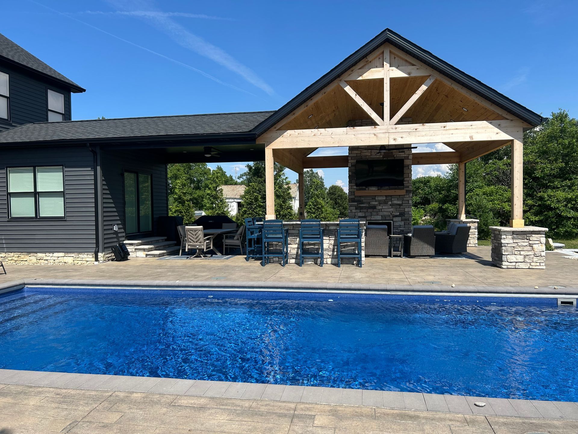 Poolside outdoor living area with pool, covered patio, outdoor kitchen, and blue chairs.