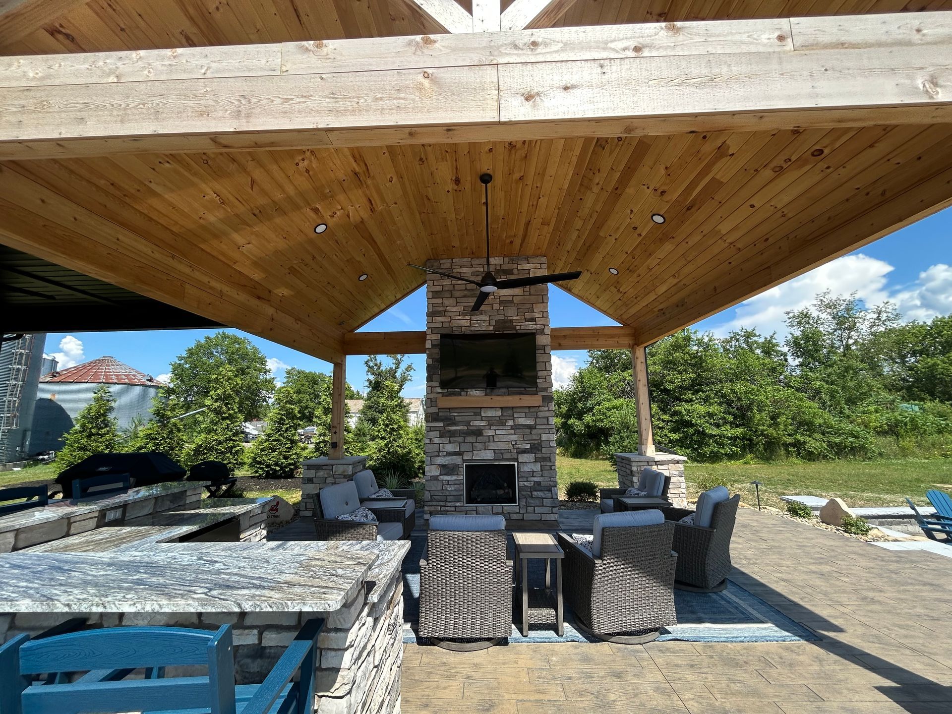 Outdoor patio with fireplace, TV, seating, and overhead wooden beam structure.