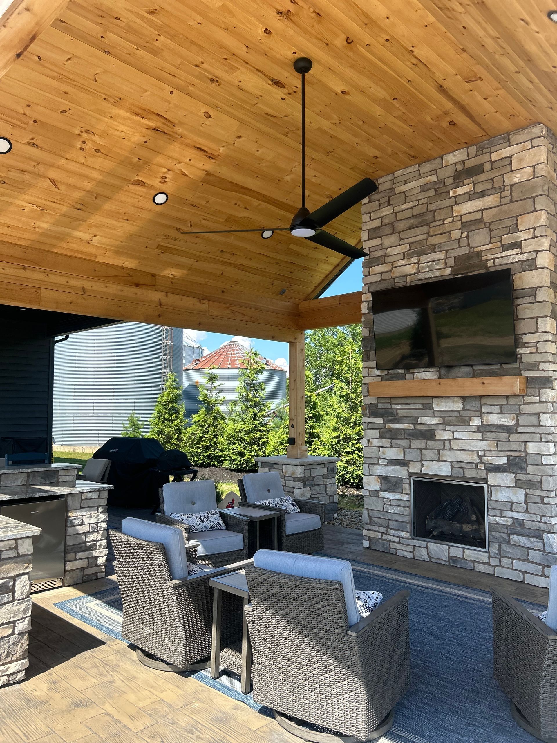 Outdoor patio with stone fireplace, grill, seating, and ceiling fan.