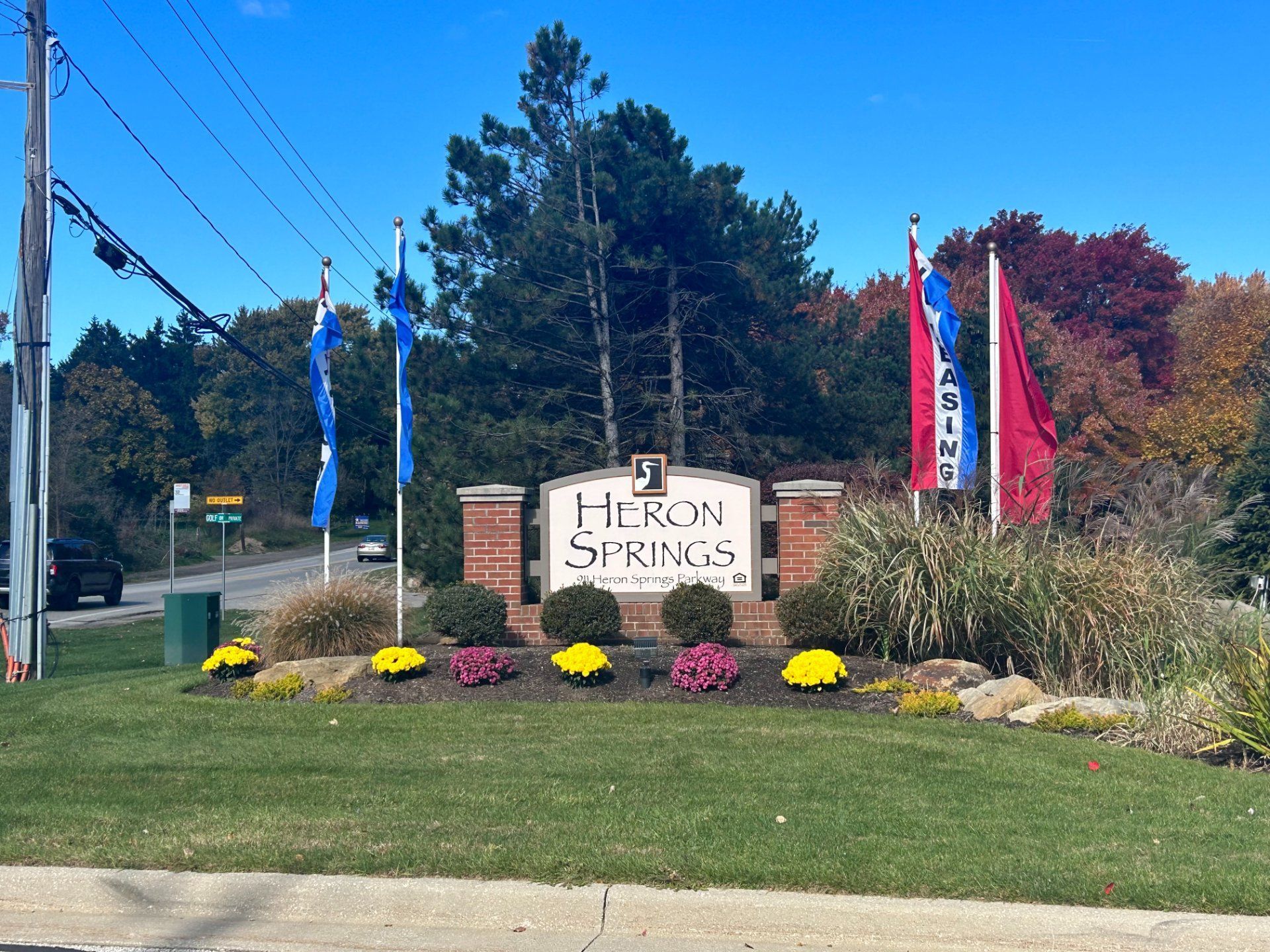 Sign for Heron Springs apartments with flags and landscaping.
