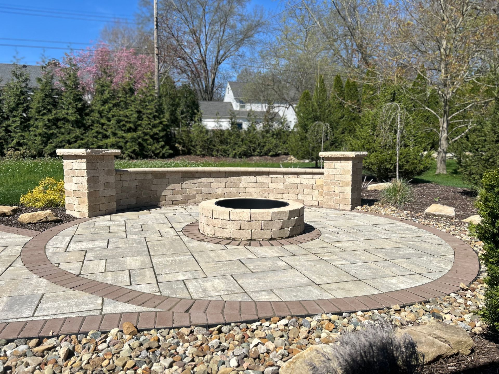 Circular stone patio with fire pit, seating wall, and surrounding landscaping.