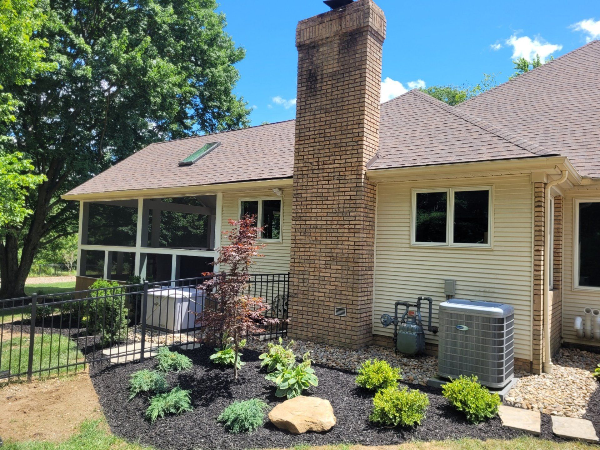 Back exterior of house with a screened porch, chimney, and landscaped garden with black mulch.