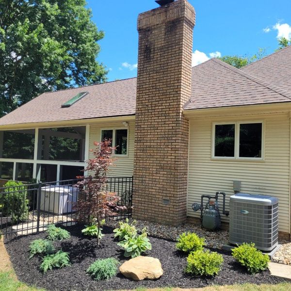 Backyard view of a house with brick chimney, black mulch flower bed, and air conditioning unit.