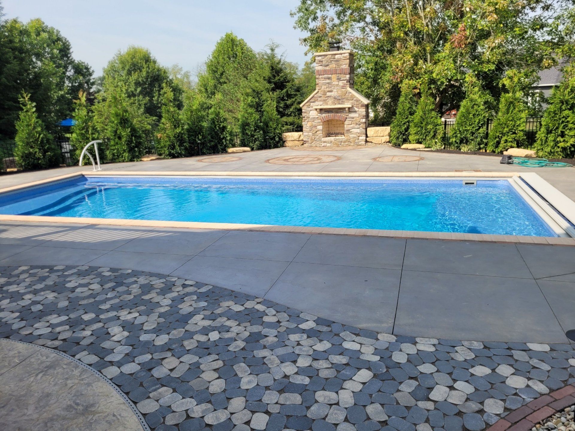 Outdoor swimming pool with blue water, concrete deck, and stone fireplace in the background.