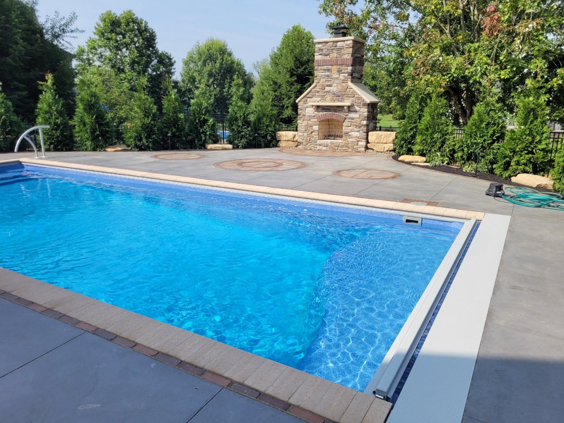 Swimming pool with blue water and stone fireplace in backyard setting.