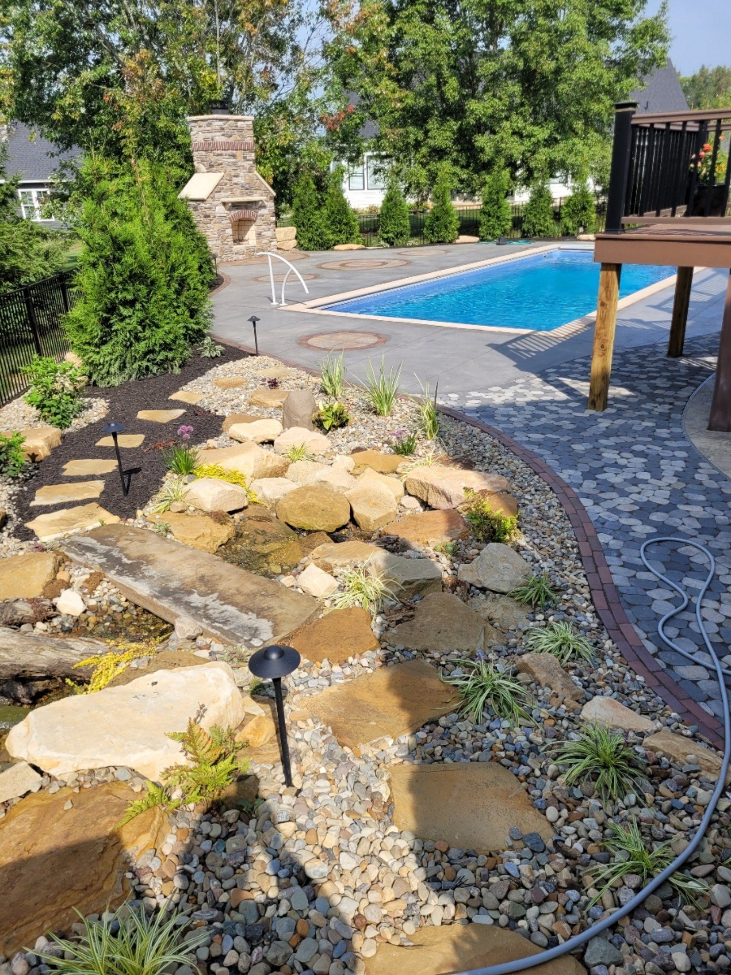Backyard patio with a pool, garden, fireplace, and deck. Stone path leads from garden to pool.