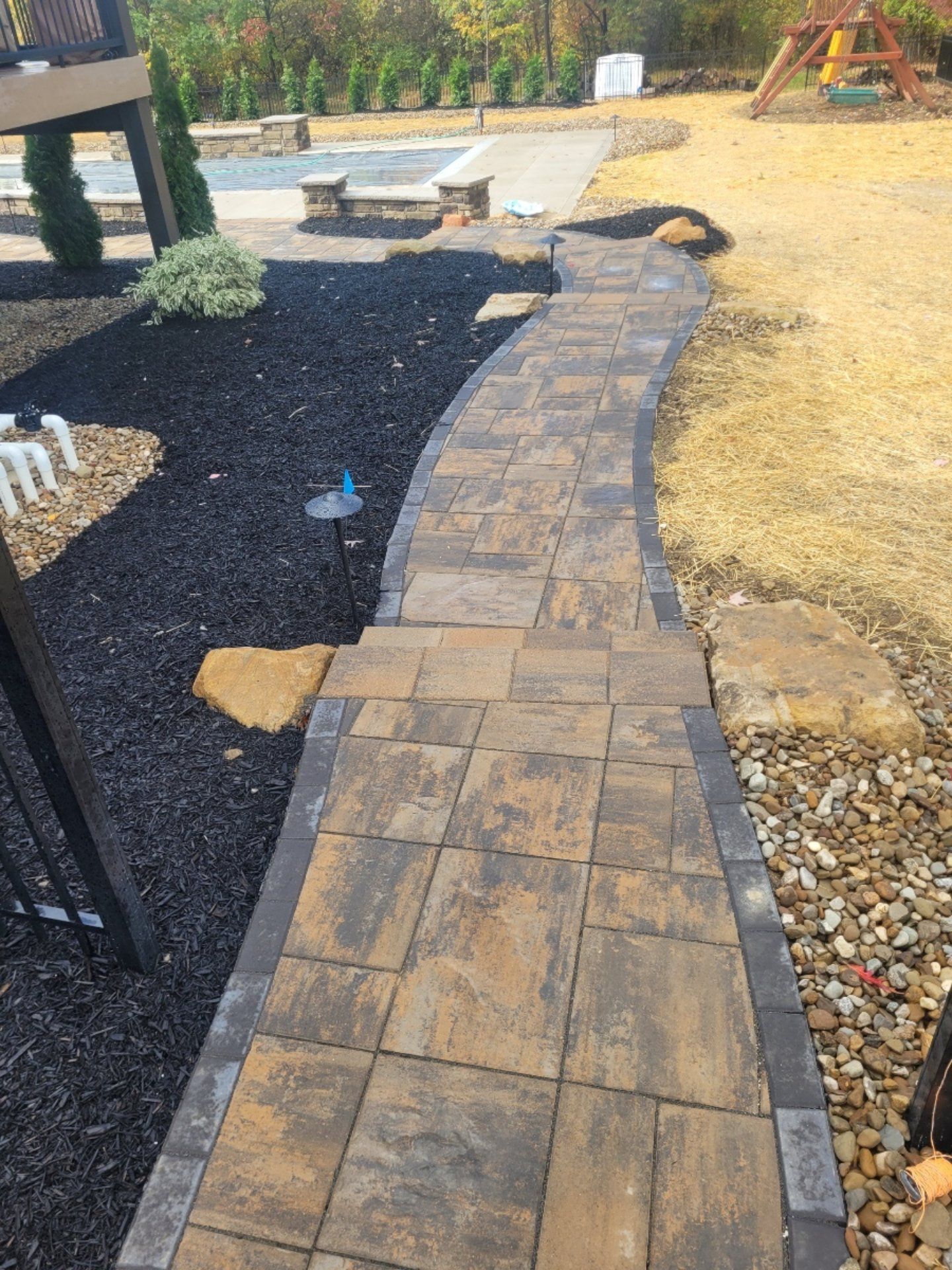 Brick pathway winding through a yard with black mulch and grass, leading to a playground.