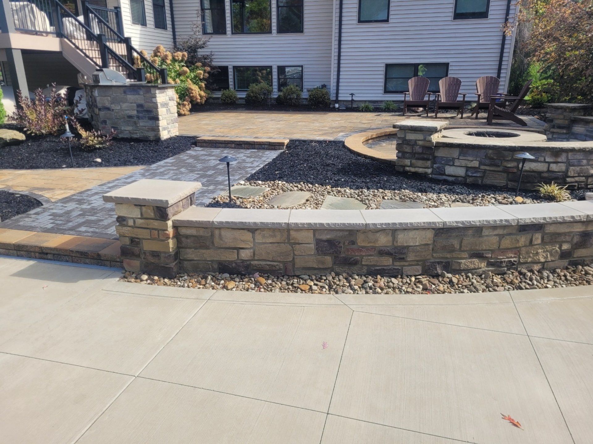 Stone walls border a backyard patio with a fire pit and pathway.