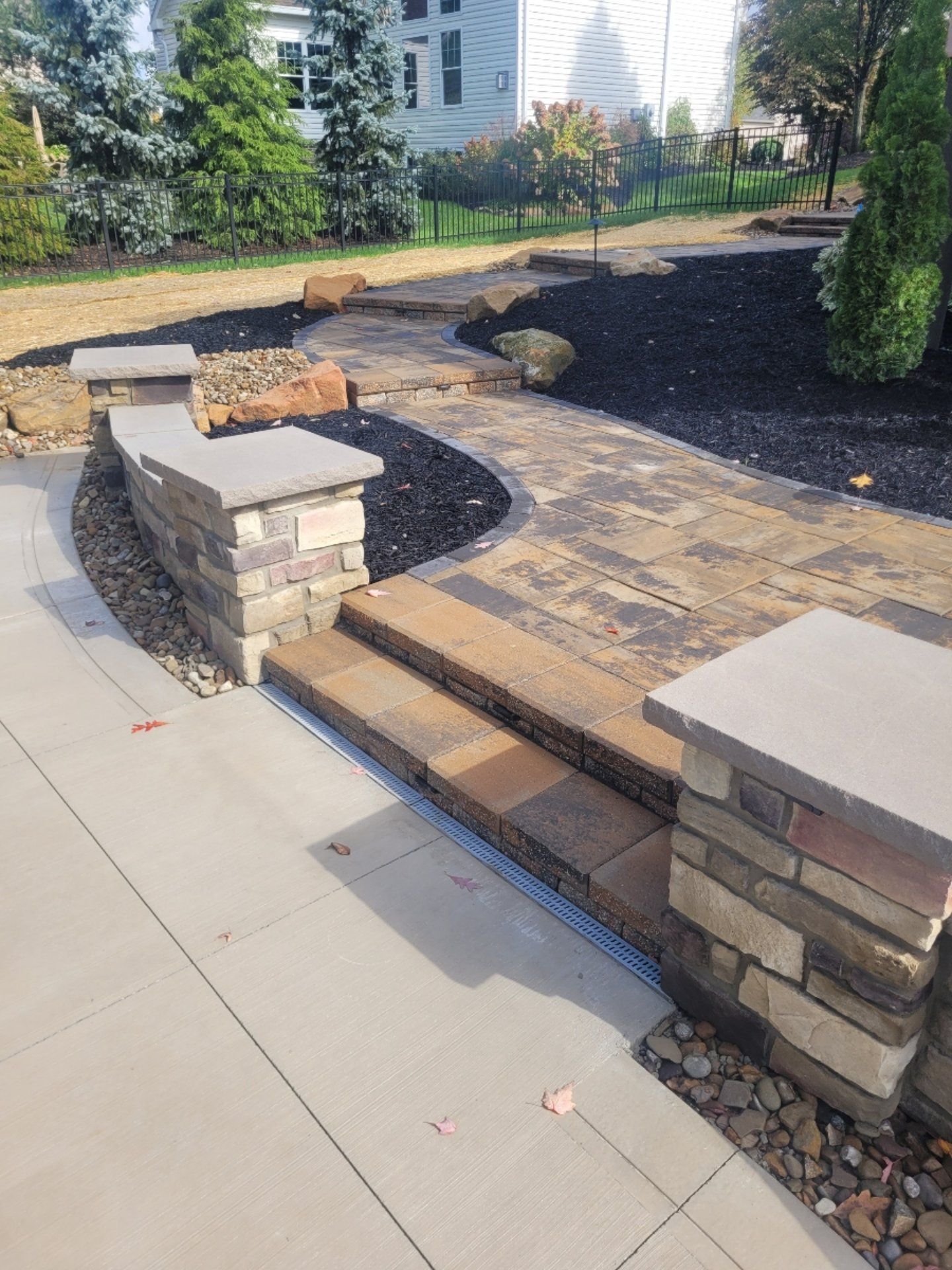 Stone walkway with steps and retaining walls, leading to a landscaped area with mulch and trees.