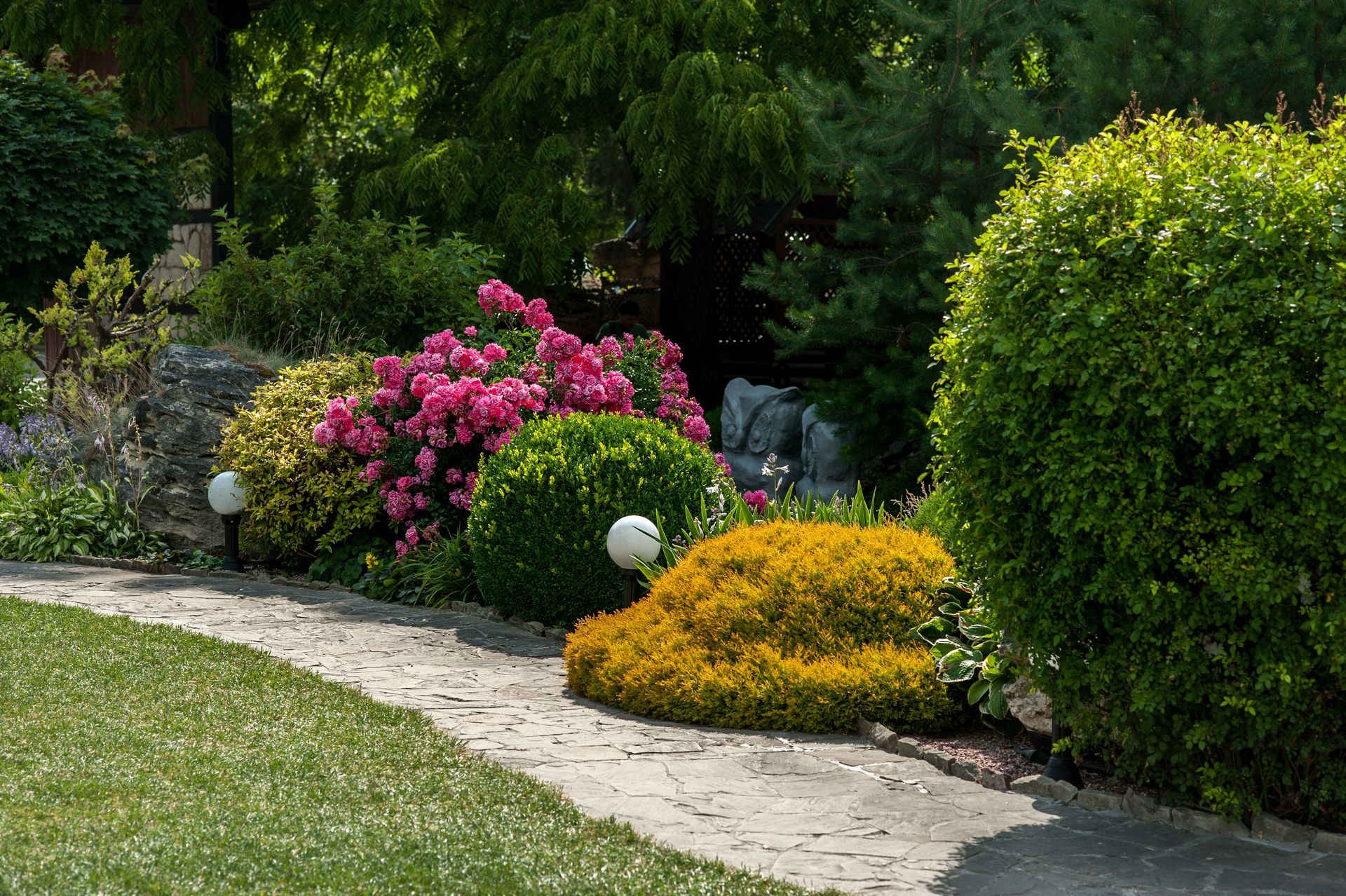 Stone path winds through a garden of colorful bushes and flowering shrubs.