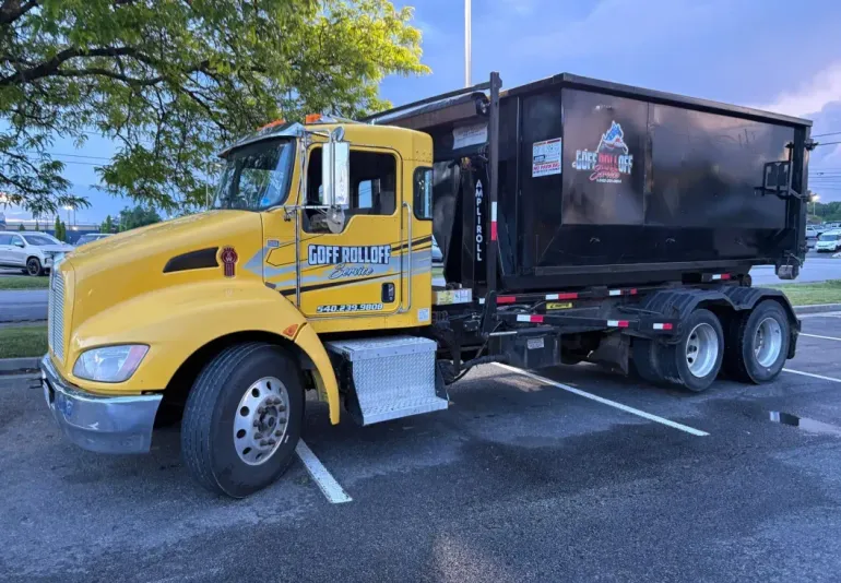 Flatbed truck and trailer parked in a lot with orange traffic cones beside apartment buildings