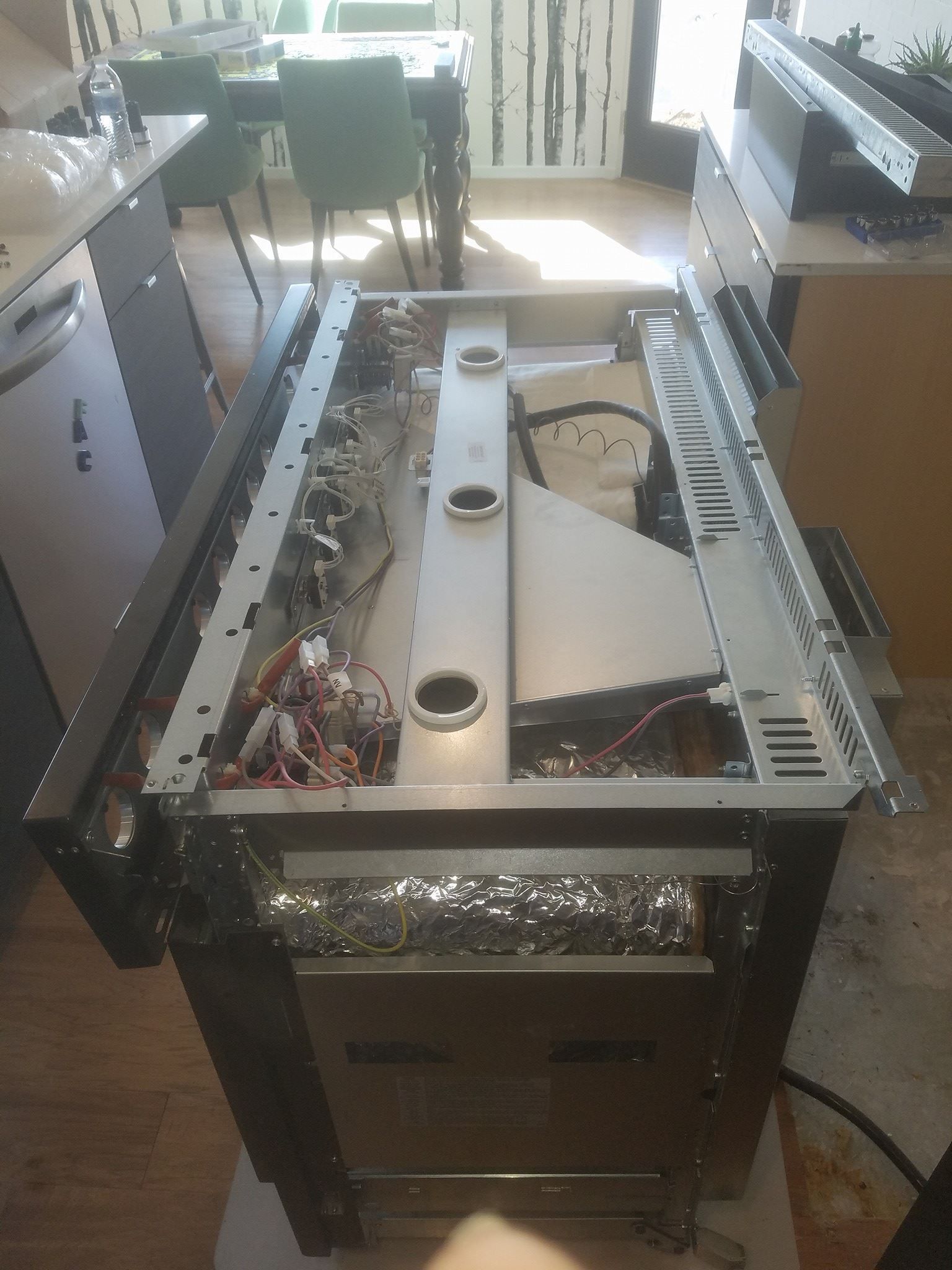 Damaged metal appliance or machine with exposed wiring and removed panels in a kitchen-like room