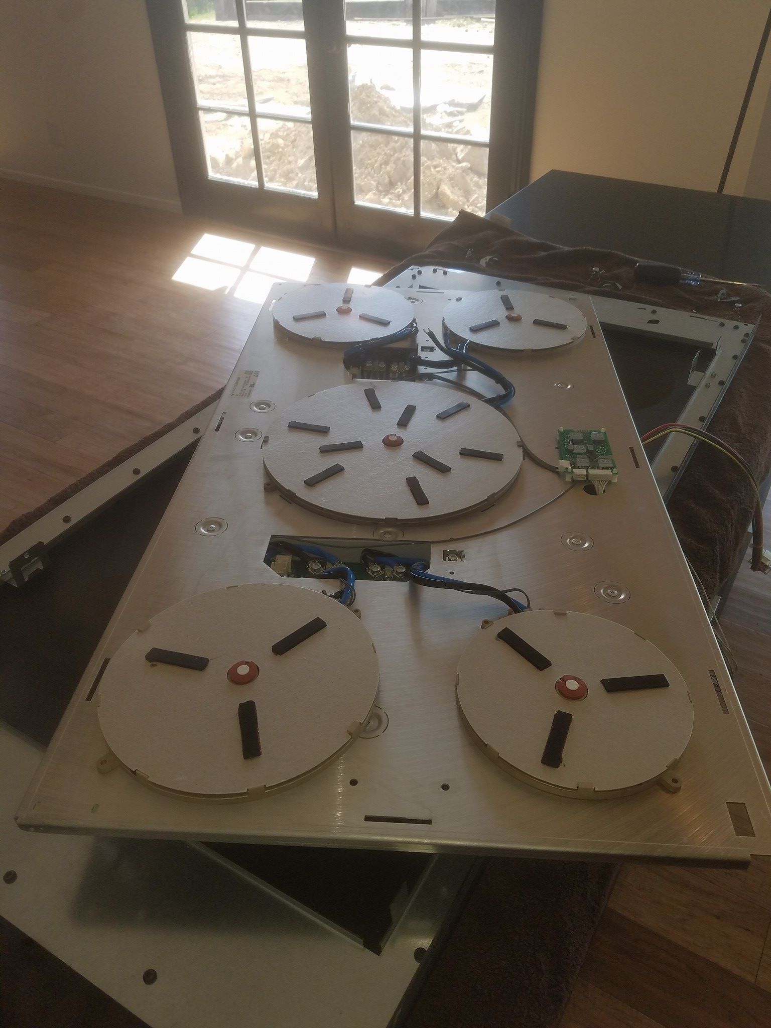Prototype tabletop robot with four white round platforms and sensors on a wooden board by a sunlit window