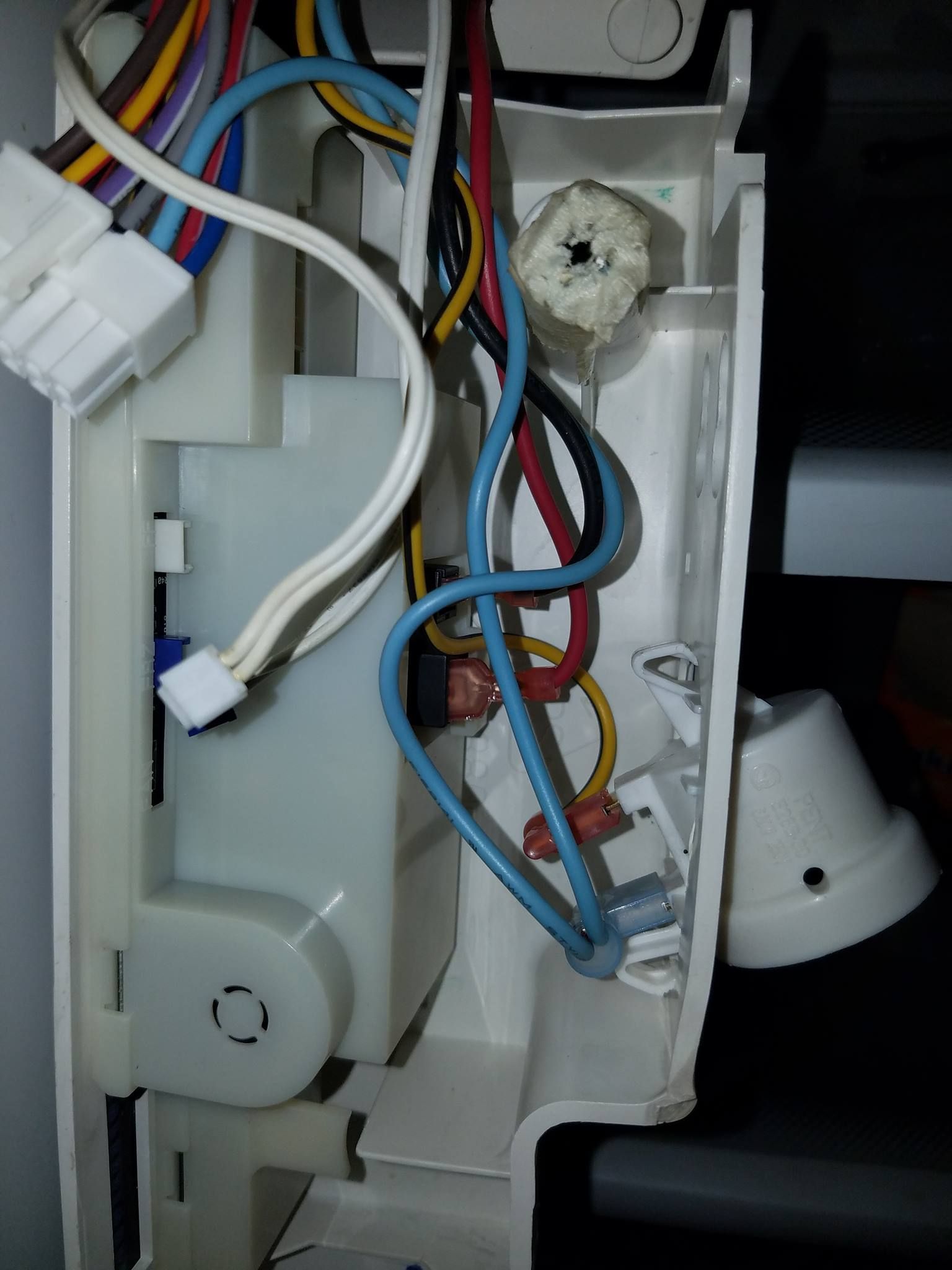 Close-up of appliance wiring and white plastic components inside a machine cavity
