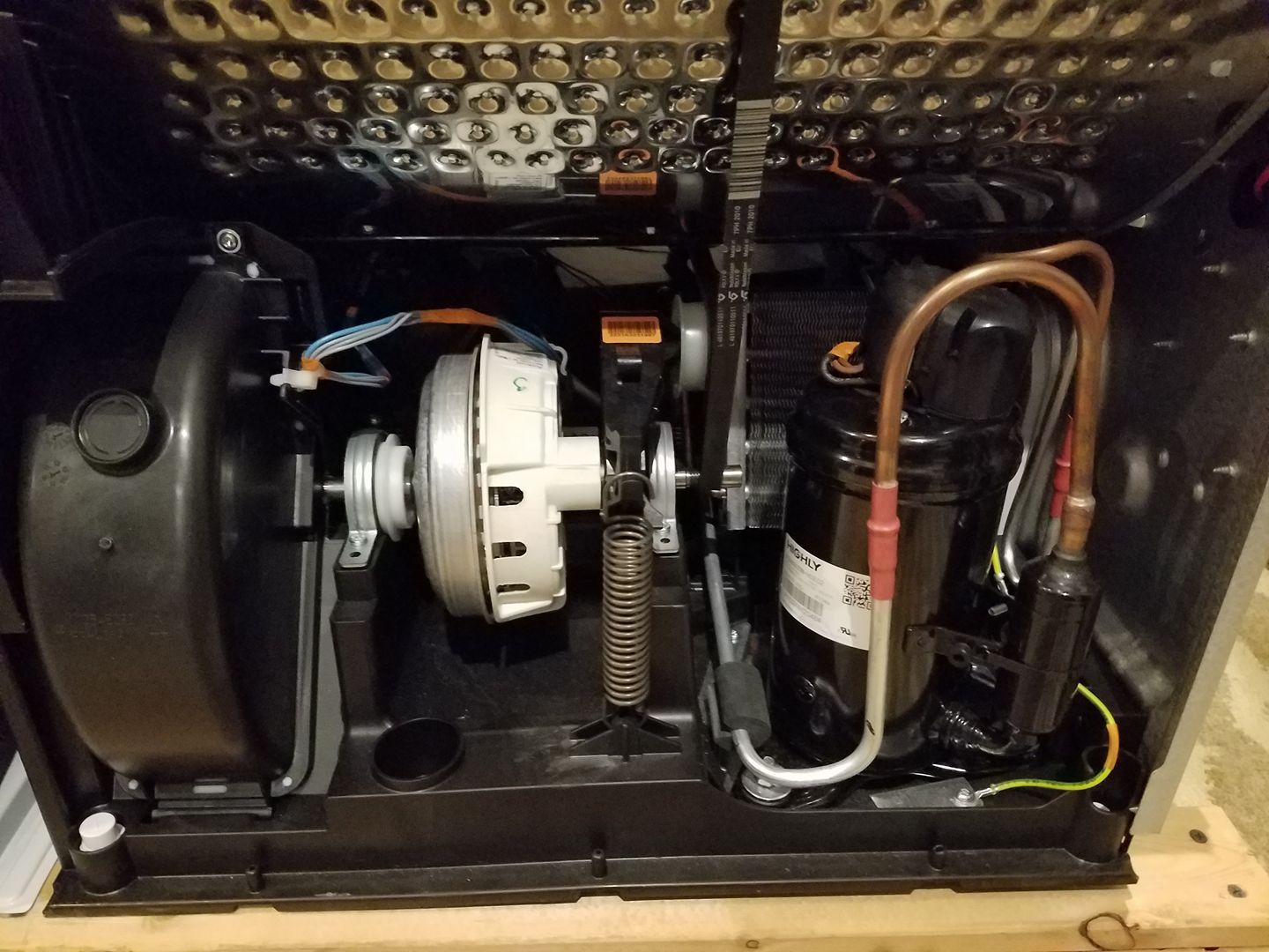 Close-up of a machine interior with a black fan, white motor, gears, wires, and copper tubing.