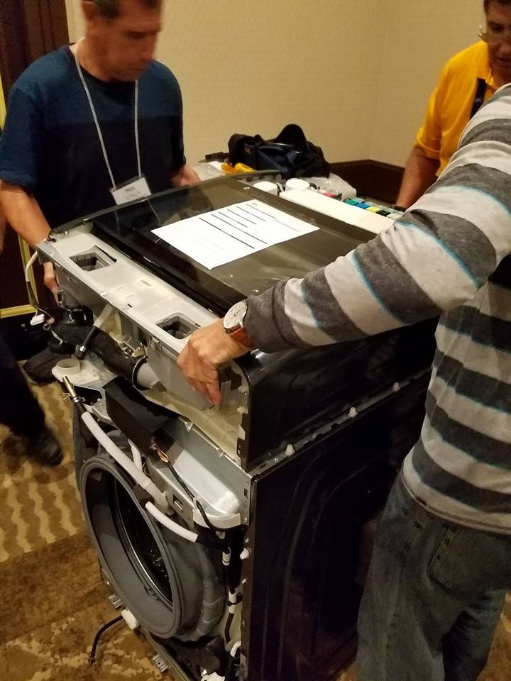 People loading a washing machine into a cart in a workshop or storage room
