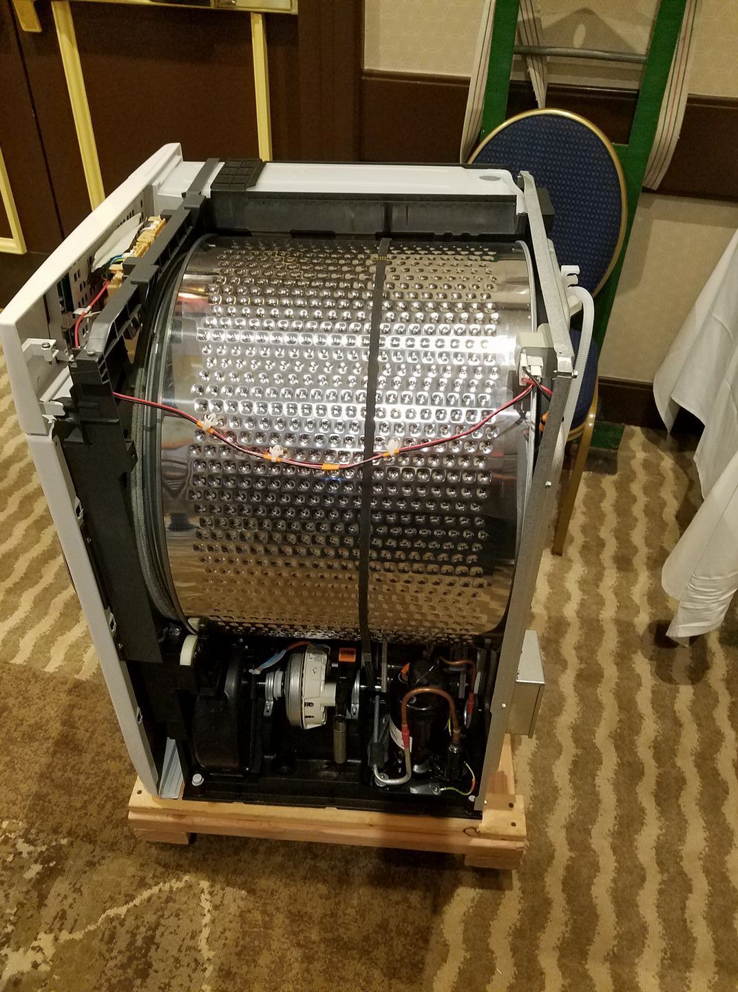 Open machine with large perforated metal drum and exposed internal components on a wooden base.