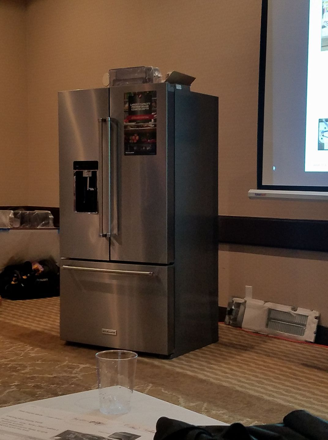 Stainless steel refrigerator in a room with a projector screen and a table in the foreground