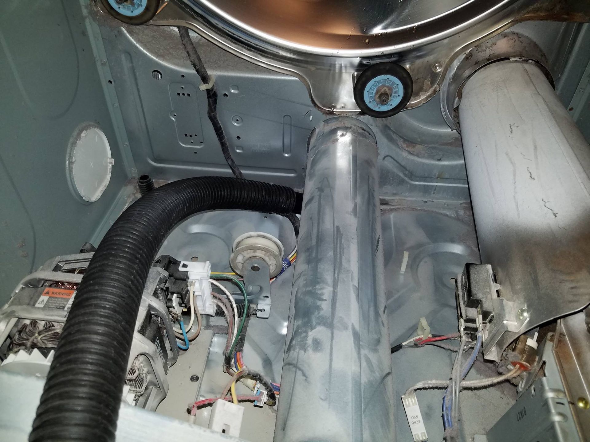 Interior of a washing machine with visible drum, hoses, wiring, and metal housing panels