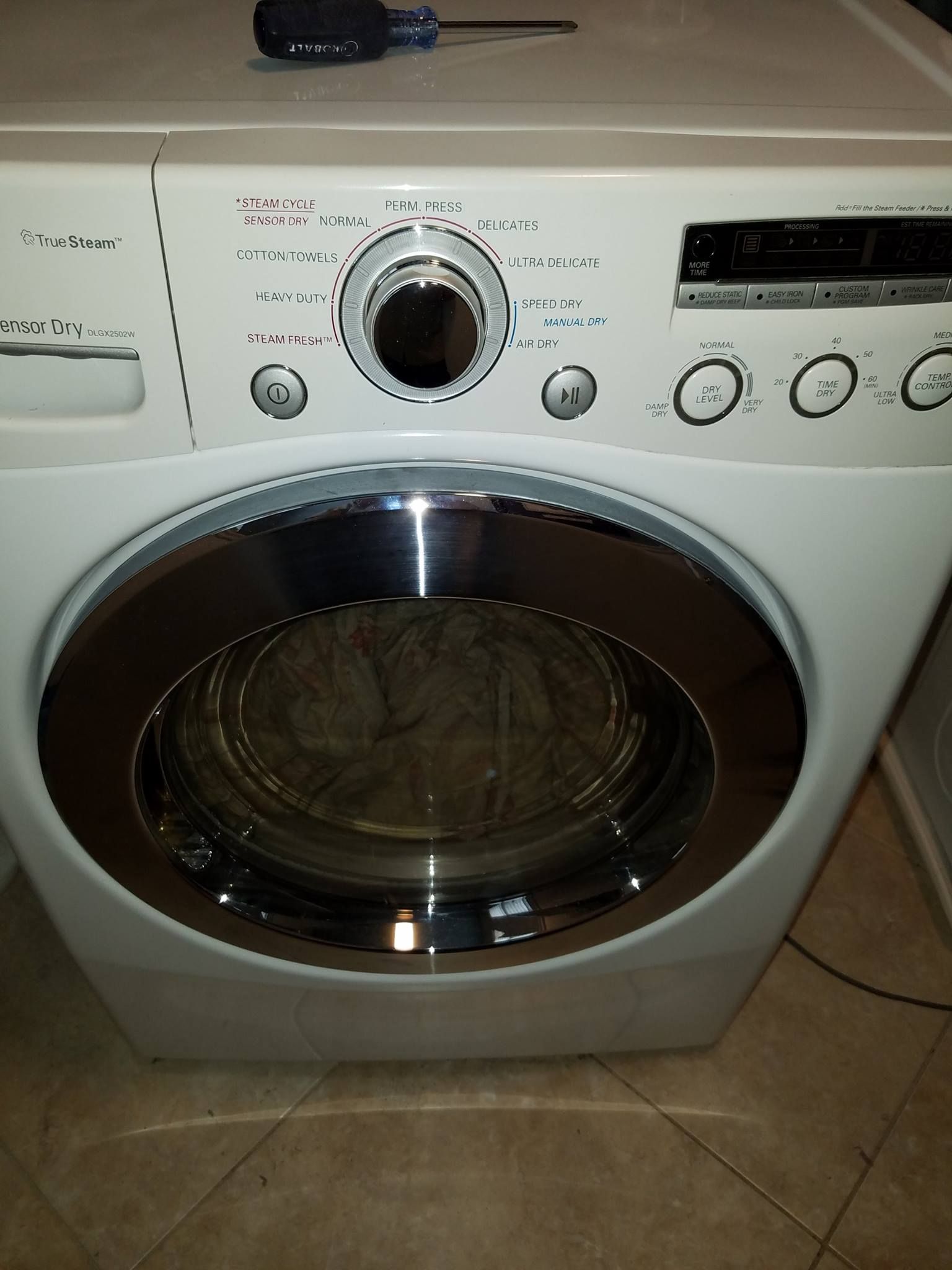 White front-loading washer/dryer with black door and control knobs on a tiled floor