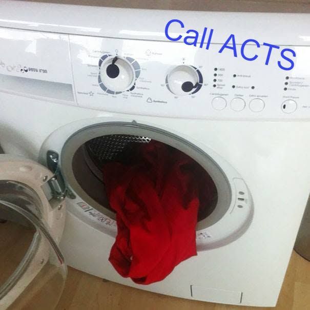 Red clothes in a front-loading washing machine with the door open and “Call ACTS” written above the controls