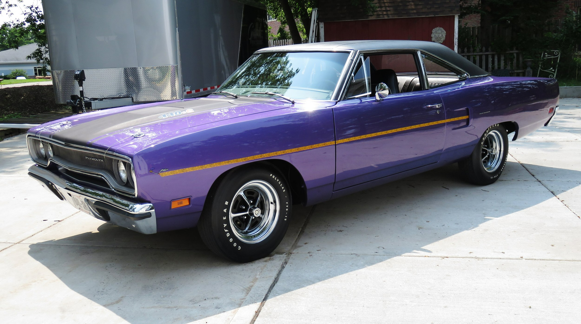 A purple car is parked in a driveway next to a trailer