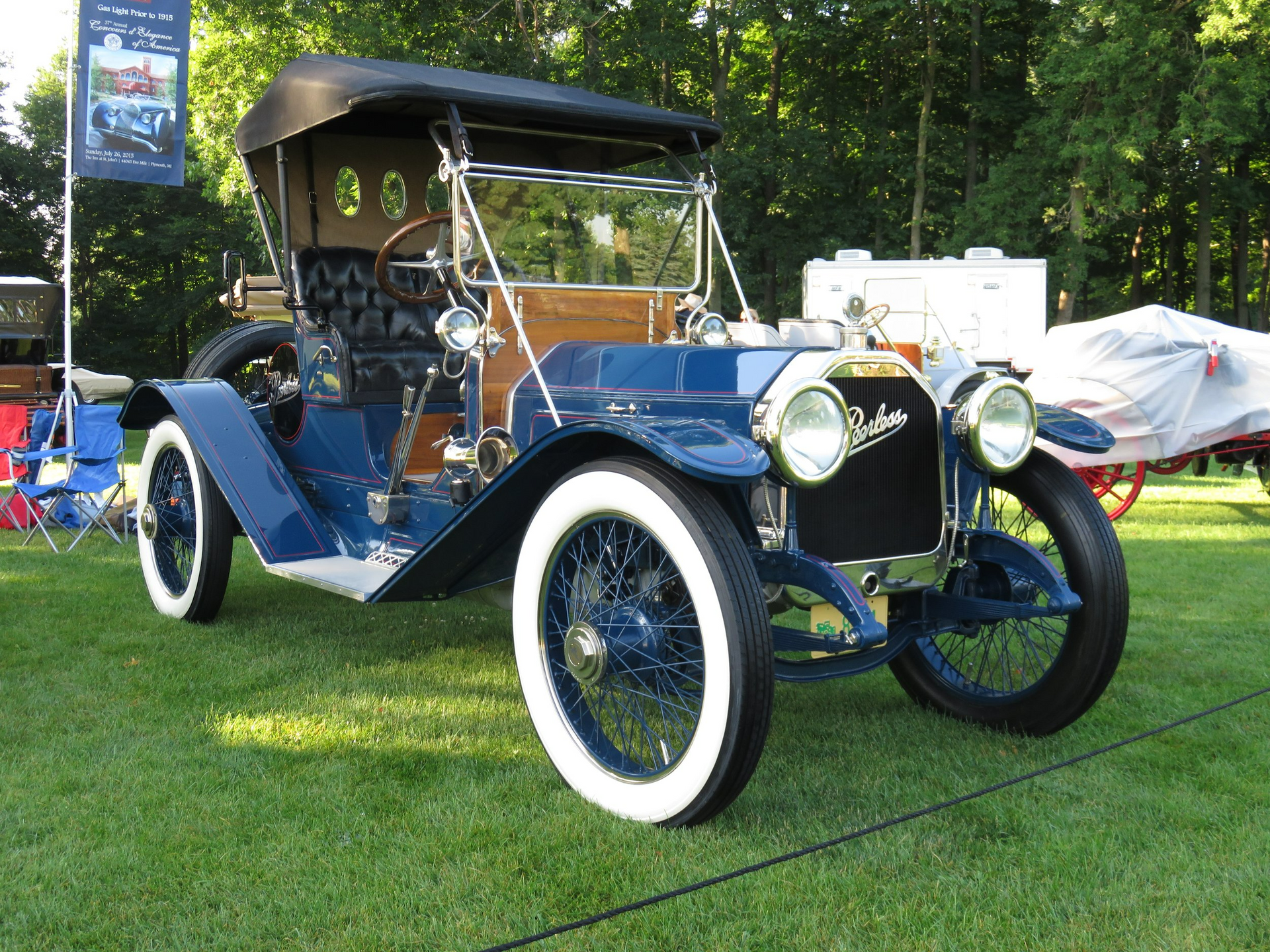 An old blue car with white tires is parked in the grass.