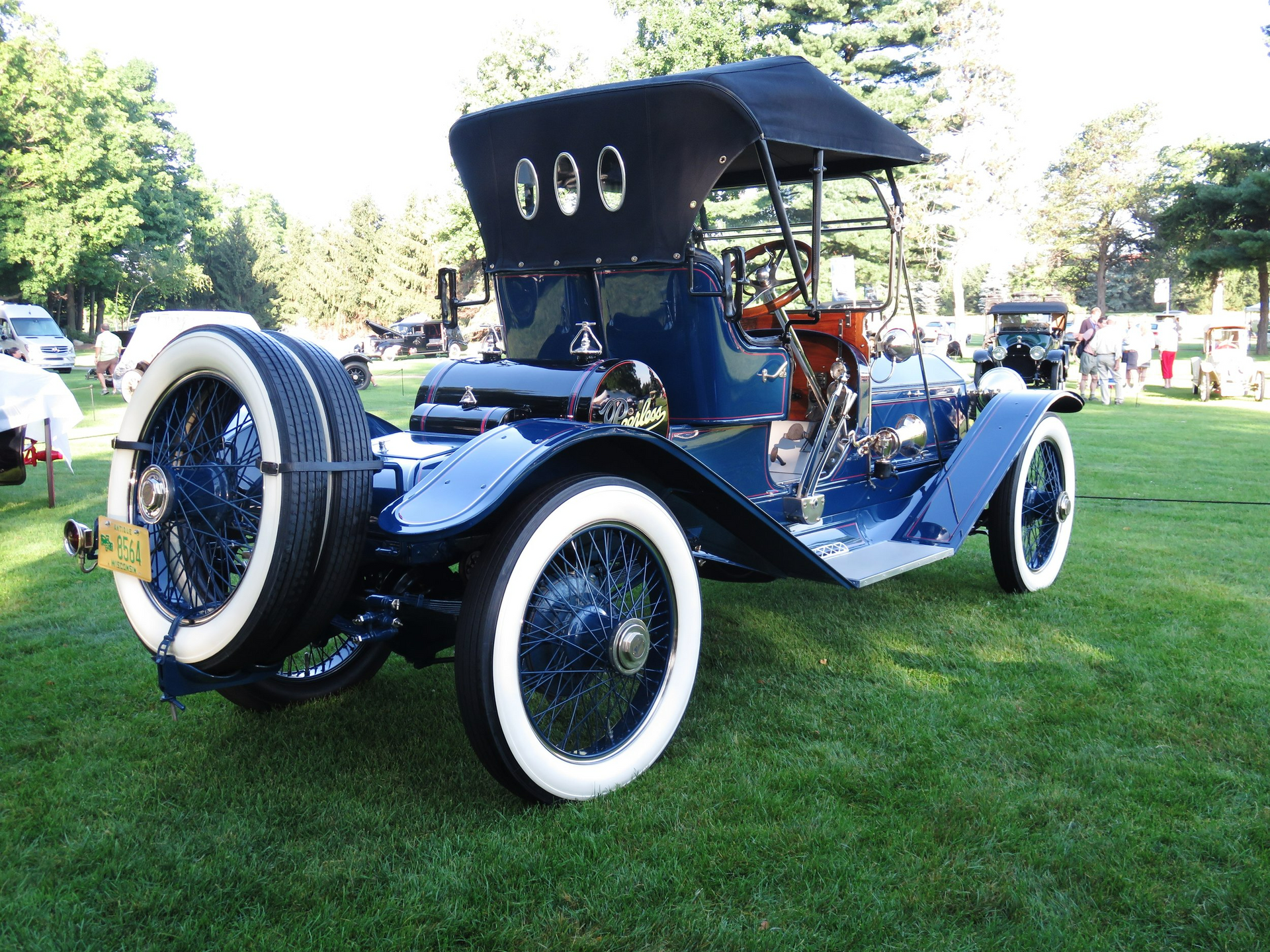 A blue car with white tires is parked in the grass