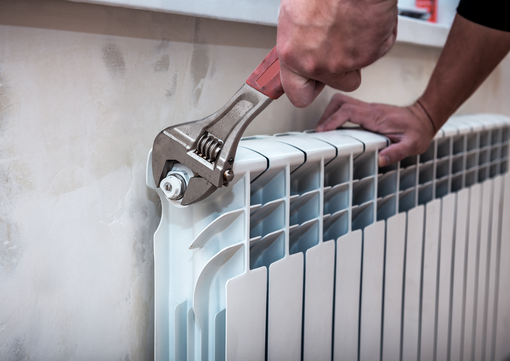 Hands using an adjustable wrench to tighten a valve on a white radiator.