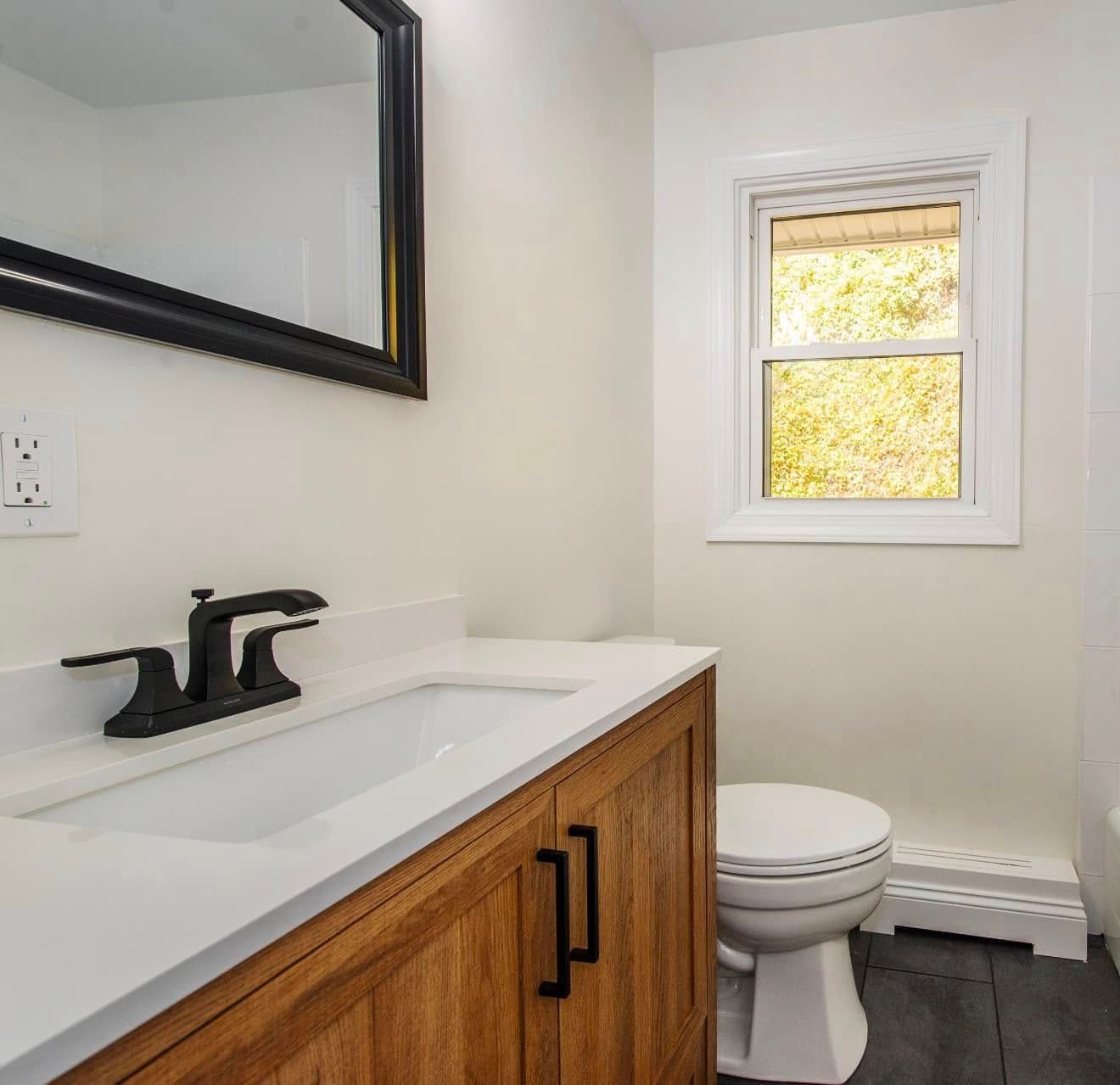 A bathroom with a sink , toilet , mirror and window