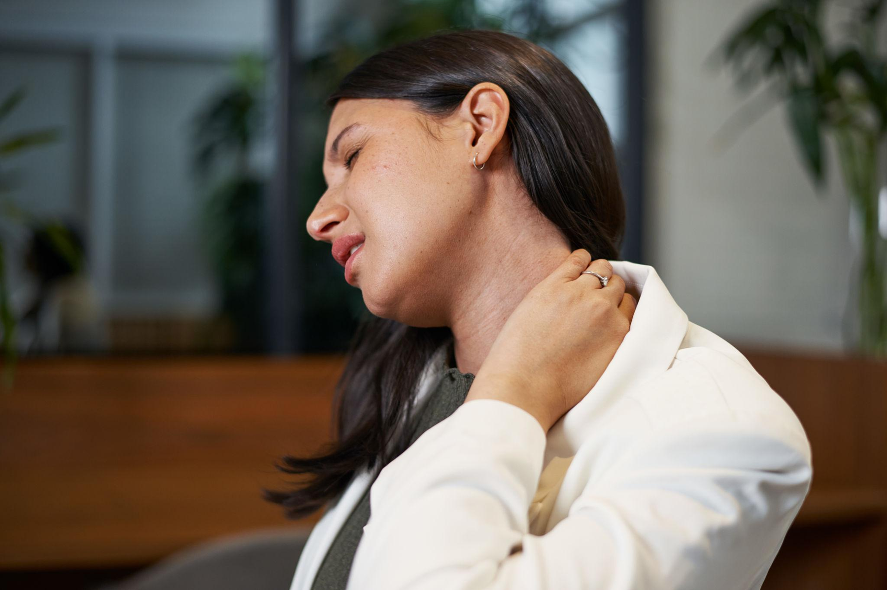 Woman in a white sweater holding her neck and looking down, appearing to feel neck pain.