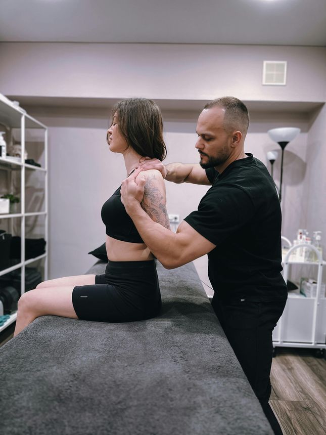 Physical therapist adjusting a seated woman’s posture on a therapy table in a clinic room