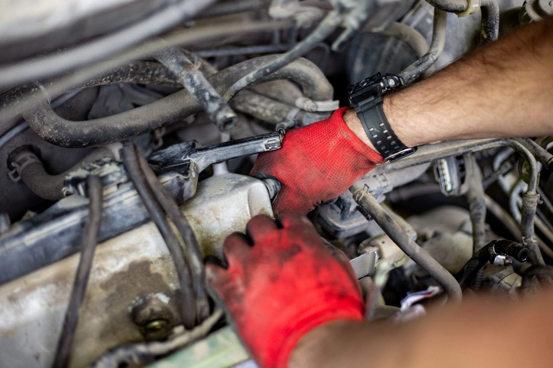 Mechanic wearing red gloves working on tangled engine wires in a car bay
