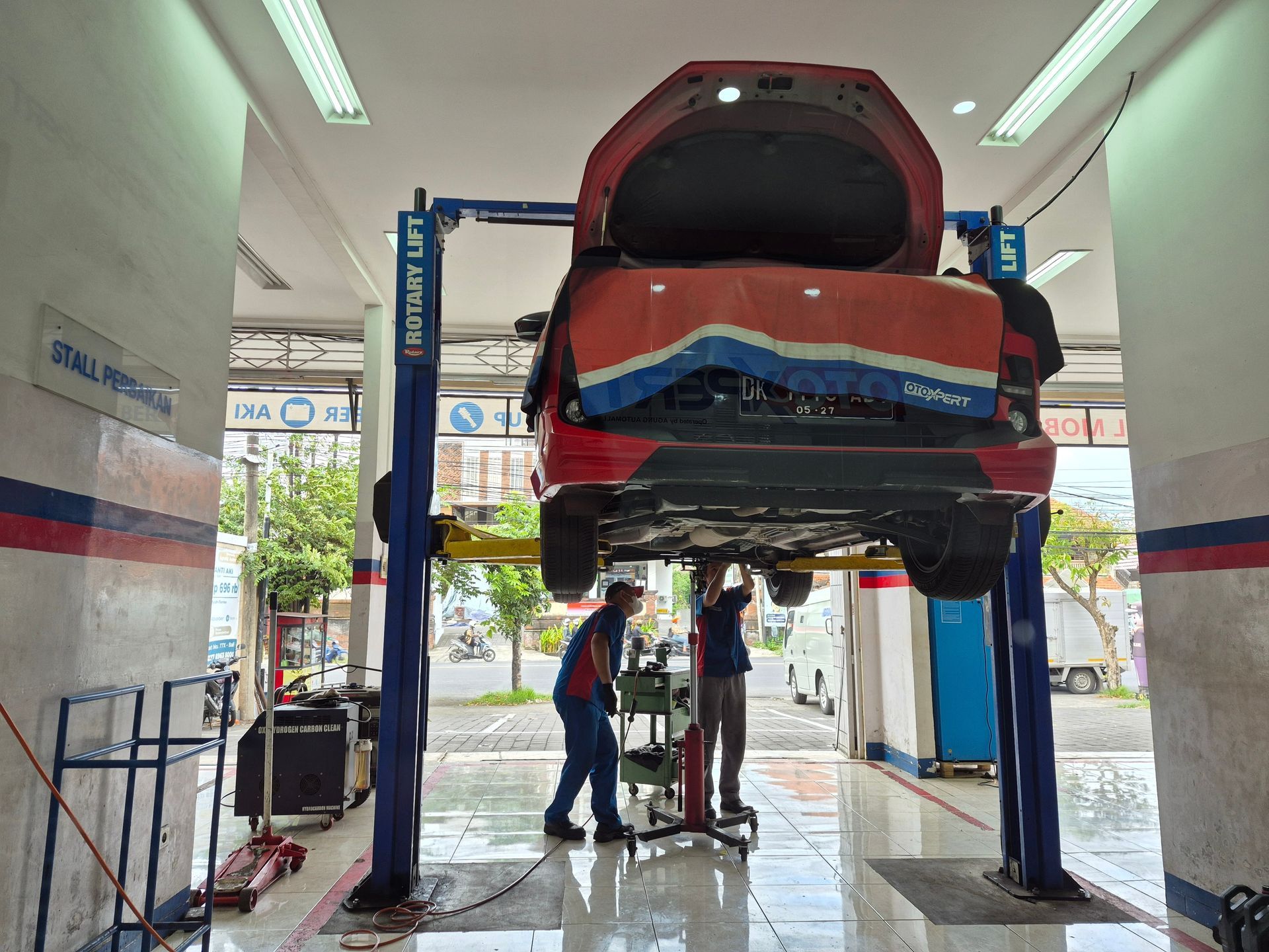 Car raised on a hydraulic lift in an auto repair shop, with a mechanic working underneath.