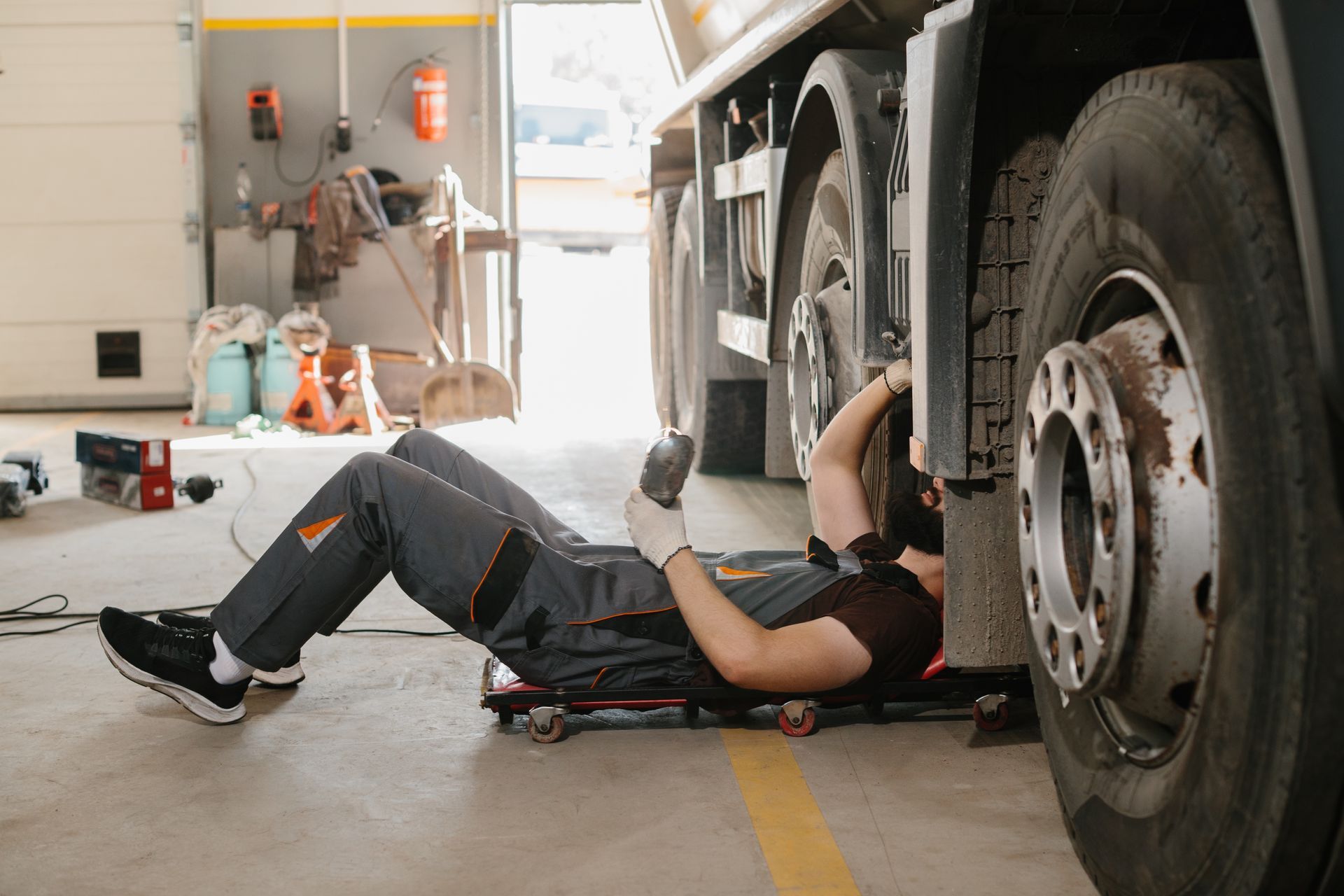 Mechanic lying under a large truck, working on the undercarriage in a garage.