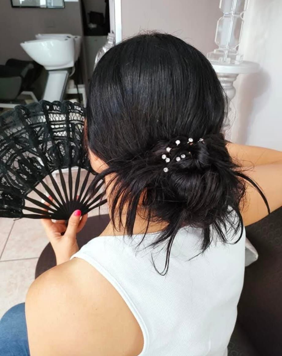 Una persona con i capelli scuri raccolti in uno chignon basso, ornato da piccole forcine floreali bianche, tiene in mano un ventaglio nero pieghevole, vista di spalle.