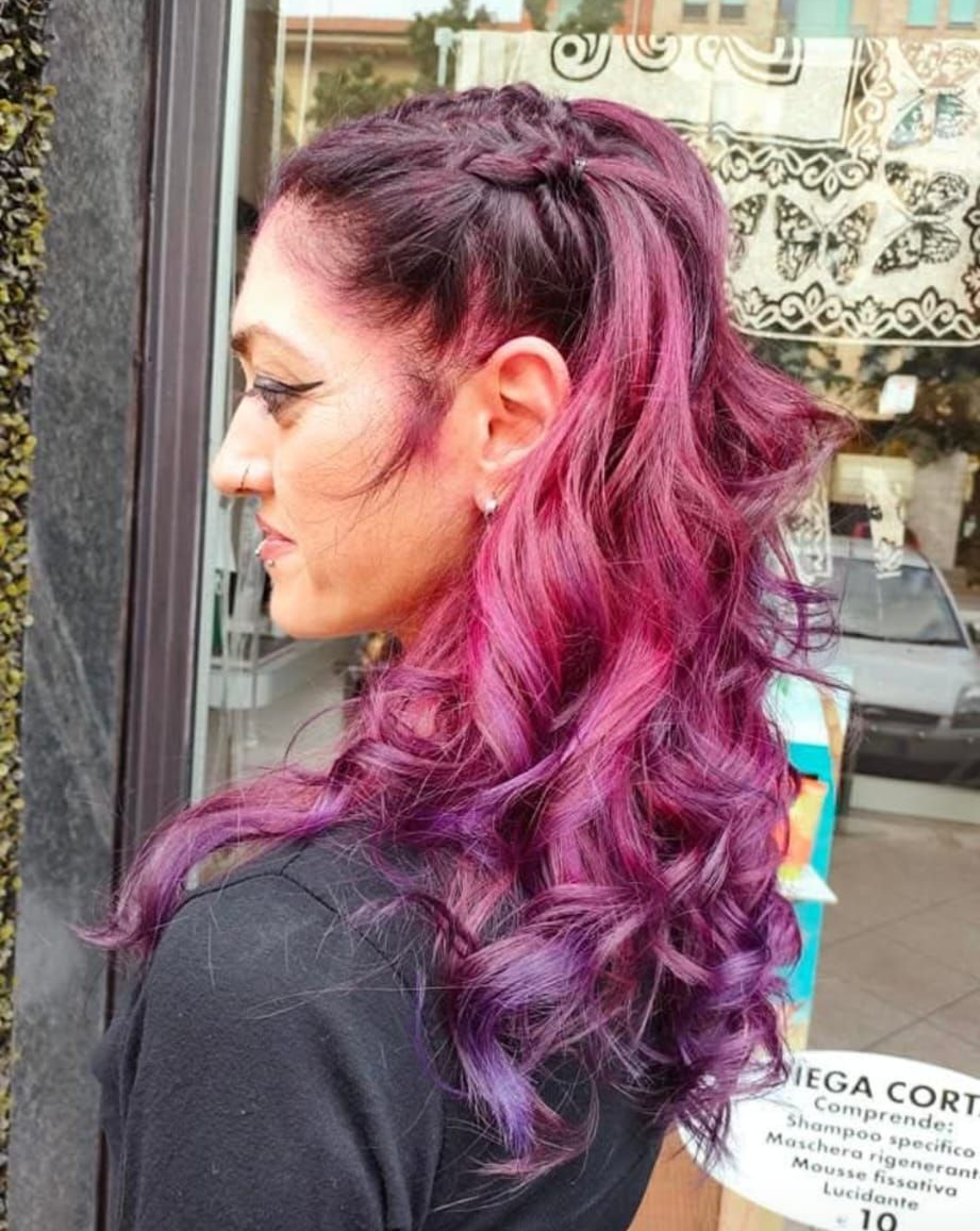 Vista di profilo di capelli mossi acconciati con una treccia laterale, caratterizzati da una vivace sfumatura che va dal magenta intenso al viola.