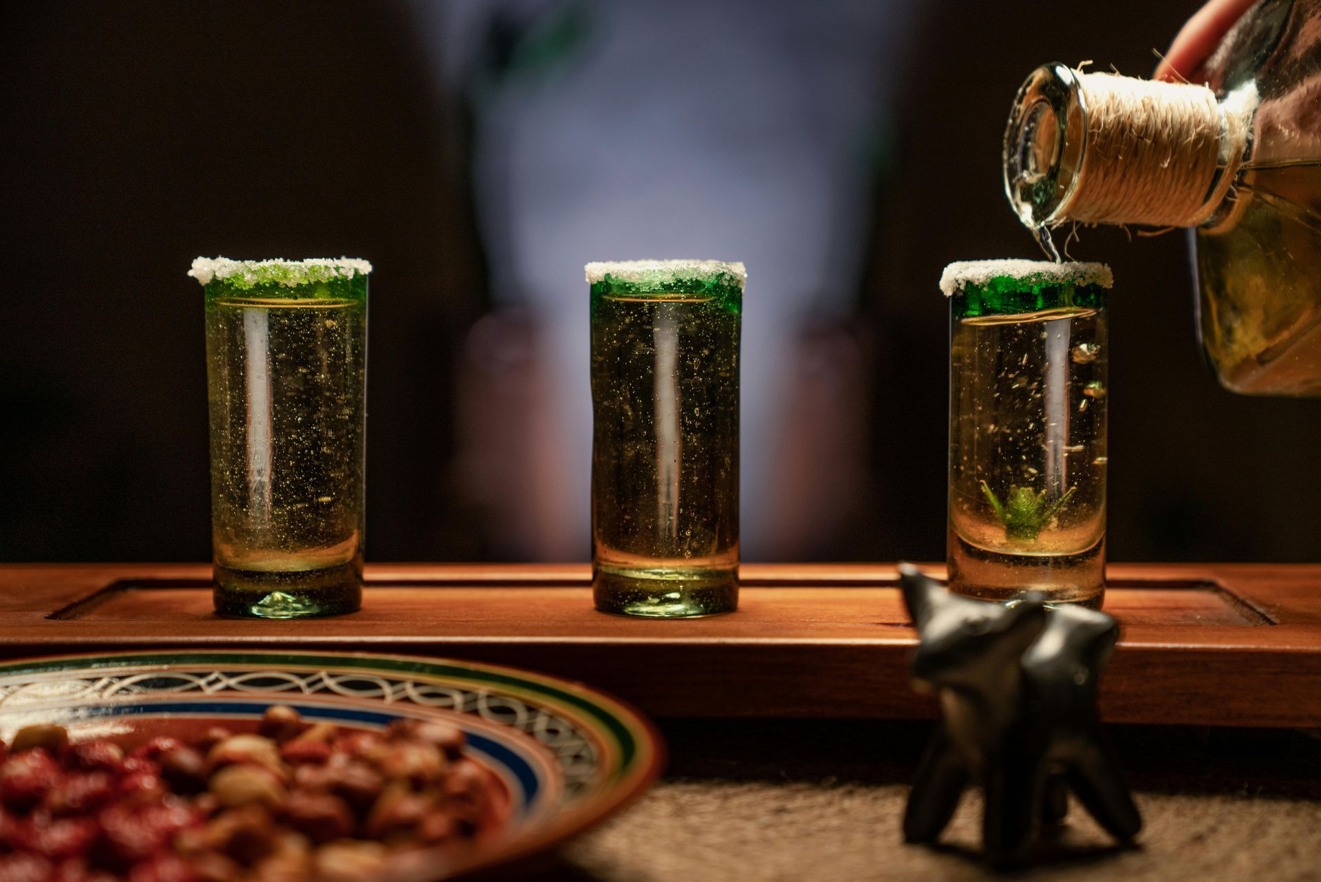 Una persona está sirviendo tequila en tres vasos de chupito sobre una mesa.