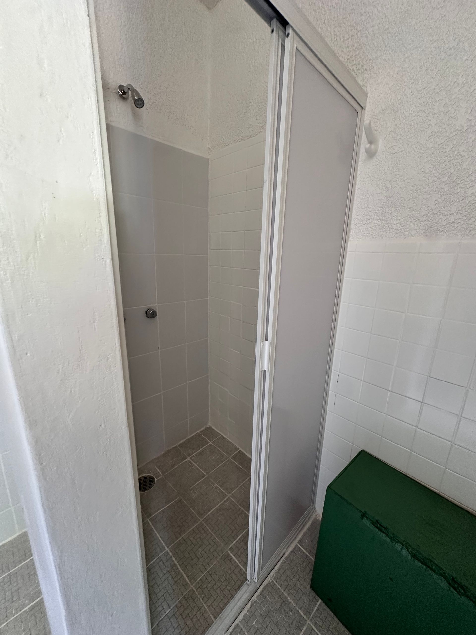 Un baño con una puerta corrediza de vidrio y un banco verde.