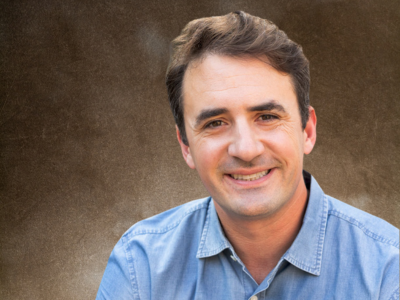 Smiling man in a blue shirt against a gray background