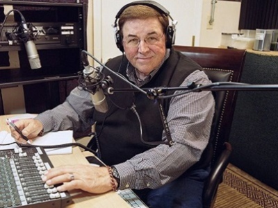 Portrait of a smiling man in glasses and a dark sweater against a blue background