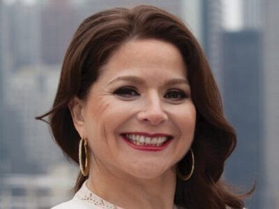 Smiling woman with brown hair and red lipstick in front of a blurred city skyline
